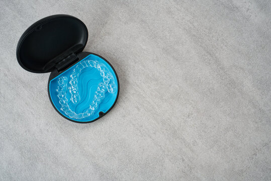 Clear dental aligner and blue case on marble table. Orthodontic mouthpiece storage.