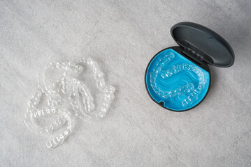 Clear dental aligner and blue case on marble table. Orthodontic mouthpiece storage.