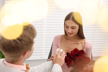 Man with engagement ring and bouquet of roses making marriage proposal to his happy girlfriend at...