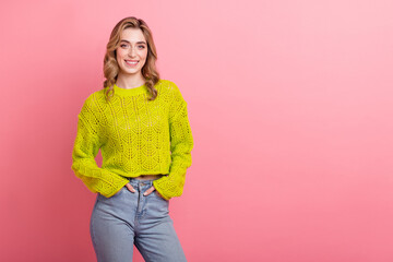 Cheerful young woman in stylish yellow sweater posing against pink background, showcasing trendy...