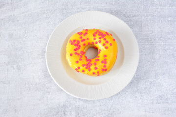 Yellow glazed donut with pink sprinkles on a white plate