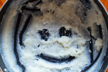 A pot with the remains of semolina porridge, on the bottom of which a smile made of semolina is...
