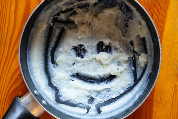 A pot with the remains of semolina porridge, on the bottom of which a smile made of semolina is drawn, creating a fun drawing on the theme of baby food