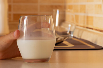 Child boy hand holding glass of milk on kitchen table against light tile background