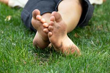 In summer on green grass in Ukraine little boy lies barefoot with dirty feet © Виктория Котлярчук