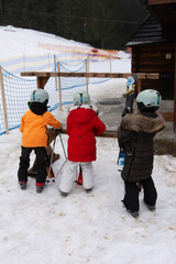 Children prepare for a day of skiing in snowy mountains, eagerly awaiting the lift while bundled in...