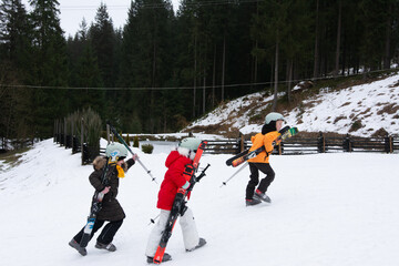 Excited children carrying skis as they head up the snowy slope on a winter afternoon in the...