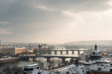 Fototapeta premium A stunning winter scene of Prague, showcasing snow-covered rooftops and bridges over the Vltava River, illuminated by soft sunlight.