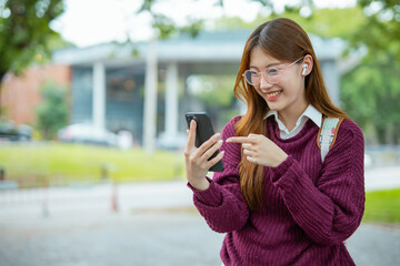  Asian female student in warm clothes using phone to chat with friends and ready for video call while in university.