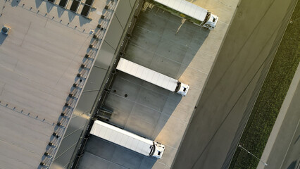 Aerial view of a distribution warehouse with three parked trucks, showcasing efficient freight logistics. Emphasizes organized cargo handling and industrial infrastructure.