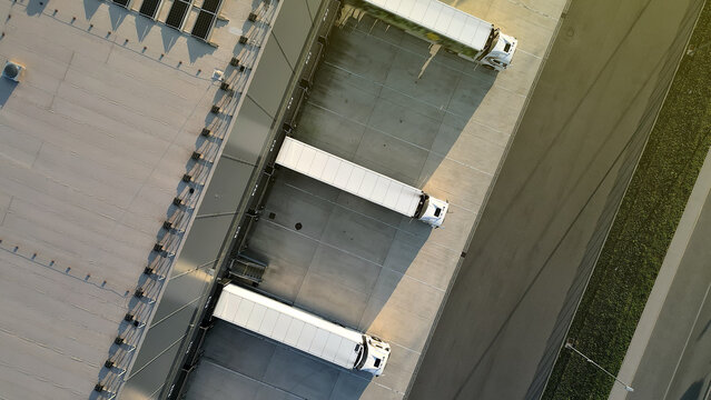Aerial view of a distribution warehouse with three parked trucks, showcasing efficient freight logistics. Emphasizes organized cargo handling and industrial infrastructure.