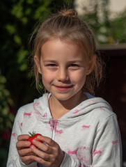 A bright sunny day in the garden, a happy caucasian girl holds a large tomato in her hands