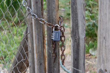 Combination padlock securing gate with rusty chain in garden setting