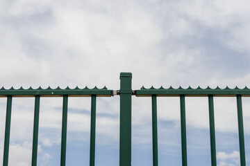 Green metal security fence with spikes protecting property under cloudy sky
