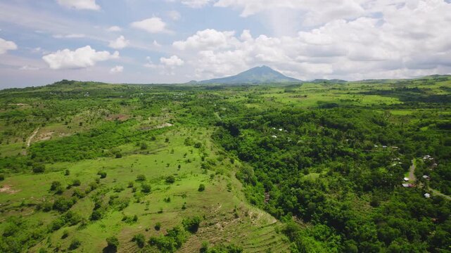 Aerial drone footage of a vast green valley in Flores island, Indonesia, with Ebu Lobo volcano mountain in the background