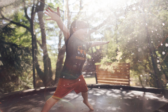 A young toddler jumps on the trampoline under a sprinkler in the summer in Oregon.