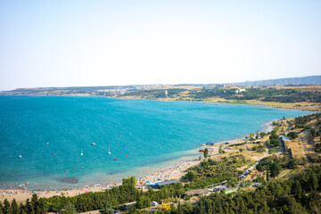 Fototapeta premium A breathtaking view of Tbilisi Sea with turquoise waters, sandy beach, and people enjoying a sunny day by the shore. The landscape combines natural beauty, rolling hills, and recreational activities