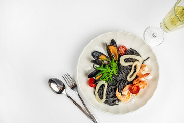Black spaghetti with seafood and arugula on a white plate. top view. copy space