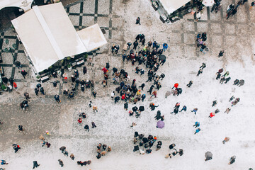 An aerial shot capturing a bustling crowd gathered in a snowy public square, surrounded by festive...