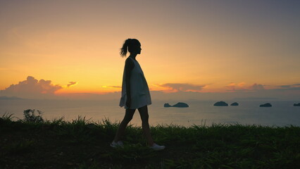 Girl relax walk tropical island sunset landscape. Green grass meadow, orange sky, small islands in...