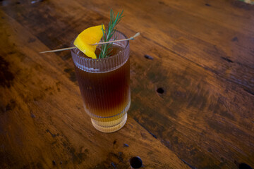 A glass of herbal tea with a sliced lemon and rosemary on an old wooden table
