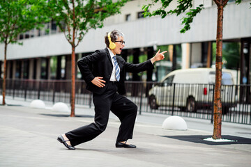 Cheerful businesswoman in formalwear dancing energetically outdoors on a city street showcasing...