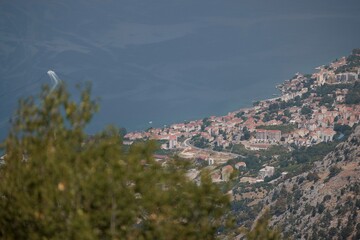 A high angle shot of a coastal European town with terracotta rooftops nestled between mountain and...