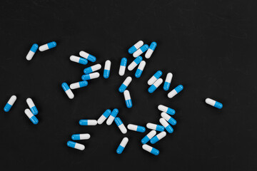 Blue and white medicine capsules pill scattered on a black background. Top view abstract pattern...