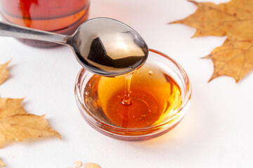Tasty golden maple syrup in bottle, bowl and spoon, with maple leaves on white background, copy space