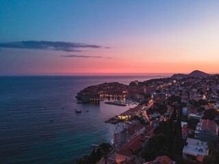 Fototapeta premium Dusk settles over the Adriatic Sea as lights begin to twinkle in the Old Town of Dubrovnik, Croatia. A beautiful sunset colors the sky with shades of pink and blue