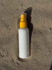 A white plastic spray bottle with a yellow cap placed on wet sand. Minimalist beach-themed composition, suitable for concepts of summer, skincare, sunscreen, vacation