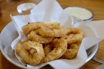 Golden fried calamari rings with lemon wedge and dipping sauces in metal bowl on wooden table. Taken at casual restaurant in Bangkok, Thailand.