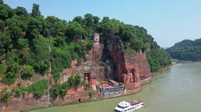 Leshan, China: Aerial drone footage of the famous Leshan giant Buddha stone statue on the Min River with tour boats in Sichuan in China. Shot with an upward motion