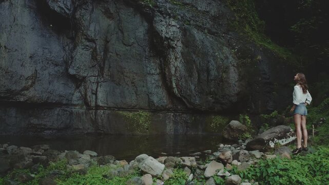 Young woman is enjoying the tranquility of nature, standing in awe of a magnificent waterfall crashing down a sheer rock face