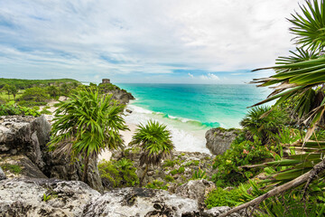 A tropical Caribbean landscape with lush vegetation, palm and rocky cliffs. The ocean waves crash against the shore, creating a picturesque scene. Tulum, Mexico. Breathtaking seascape. High-angle view
