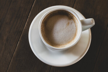 Obraz premium Hot latte coffee in white cup. Cappuccino style latte on table. Cup of latte with frothy milk. Freshly brewed latte with milk foam.