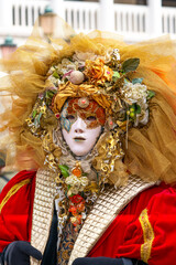 A participant wearing a golden floral mask with detailed headpiece and red costume at Venice Carnival 2025