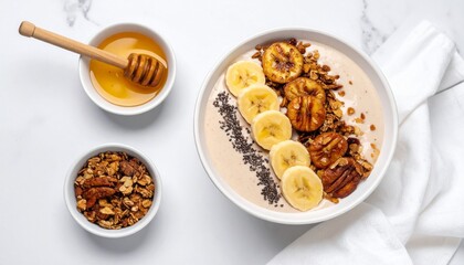 Healthy banana smoothie bowl with granola, caramelized bananas, chia seeds, and honey on white marble