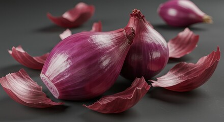 Two vibrant, red-skinned alliums rest amongst loose, papery outer layers on a dark, matte surface. One sits prominently in the foreground with another blurred nearby
