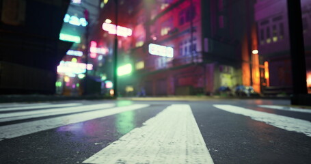 A vibrant street view features neon lights illuminating a wet urban landscape at night. The ground shows striped crosswalks, while colorful lights create a lively atmosphere.