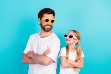 Father and daughter wearing colorful sunglass posing confidently against a bright blue background...