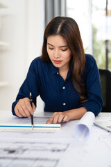 Young female engineer designer or contractor working on drawing plans and making measurements on...