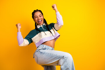Excited young woman celebrating joyfully against a vibrant yellow background wearing casual trendy...