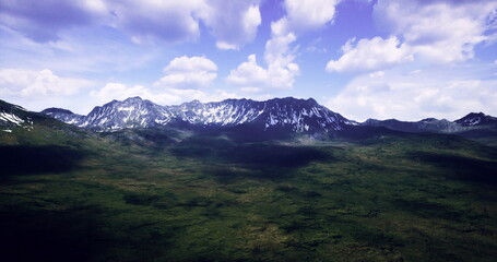 A breathtaking view of a mountain range surrounded by lush greenery. The sun illuminates the peaks while clouds float serenely above. Natures beauty on full display in a tranquil landscape.