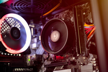 Fototapeta premium Close-up view of RGB cooling fan, CPU cooler, RAM, and colorful cables inside custom-built gaming PC with red-orange lighting. Ideal for illustrating modern computer hardware and build concepts.