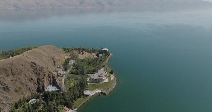 Aerial view of modern buildings nestled on the coast of Lake Sevan, where turquoise waters meet the rugged terrain, Gegharkunik Province, Armenia.