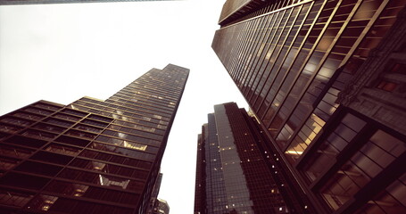 Tall skyscrapers rise dramatically from the ground, their glass facades reflecting the soft hues of dusk. The sky is overcast, creating a moody atmosphere as city life continues below.