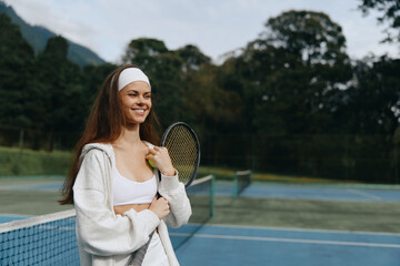 Smiling young woman in sporty attire holding a tennis racket on a sunny day at a tennis court,...