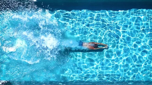 Aerial overhead slow motion view of a man jumping and diving into a swimming pool during summer time