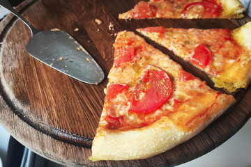 An uneaten slice of pizza with tomatoes and cheese on a wooden stand on a table in a restaurant.
